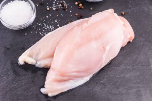 Seasoned raw chicken breasts on a cutting board