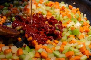A saute pan of cooked carrots, celery and onions with tomato paste and veggie stock being added