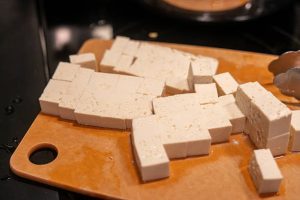 Cutting Tofu on a Wooden Board in a Kitchen Setting